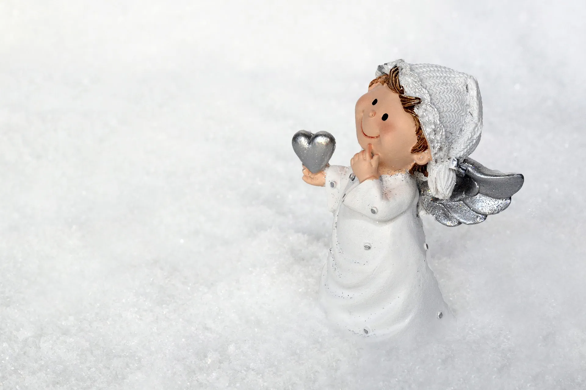 Una figurita de ángel con un corazón en la mano sobre un fondo blanco.