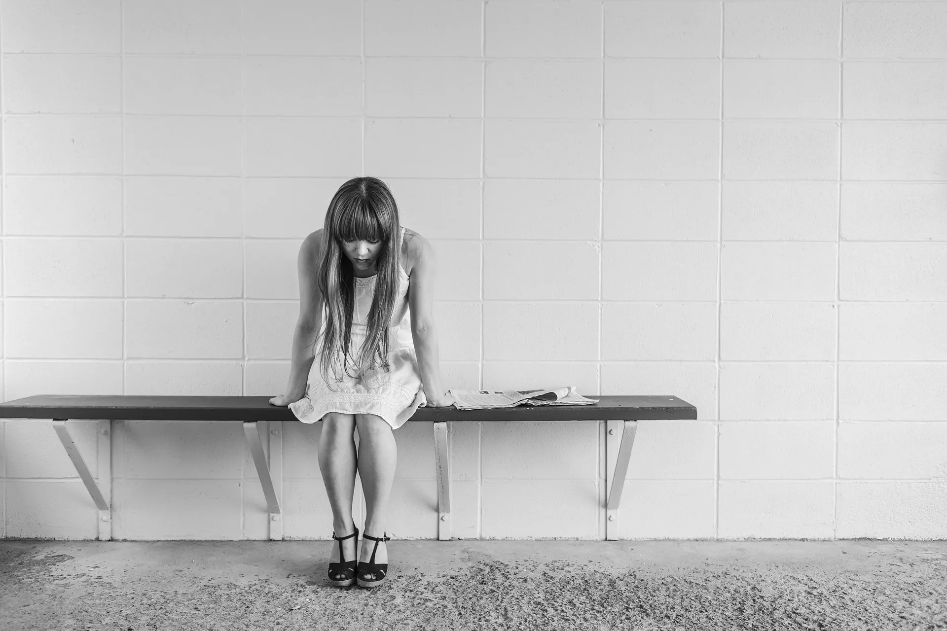 A woman sitting on a bench looks down at the ground in a black-and-white photograph.