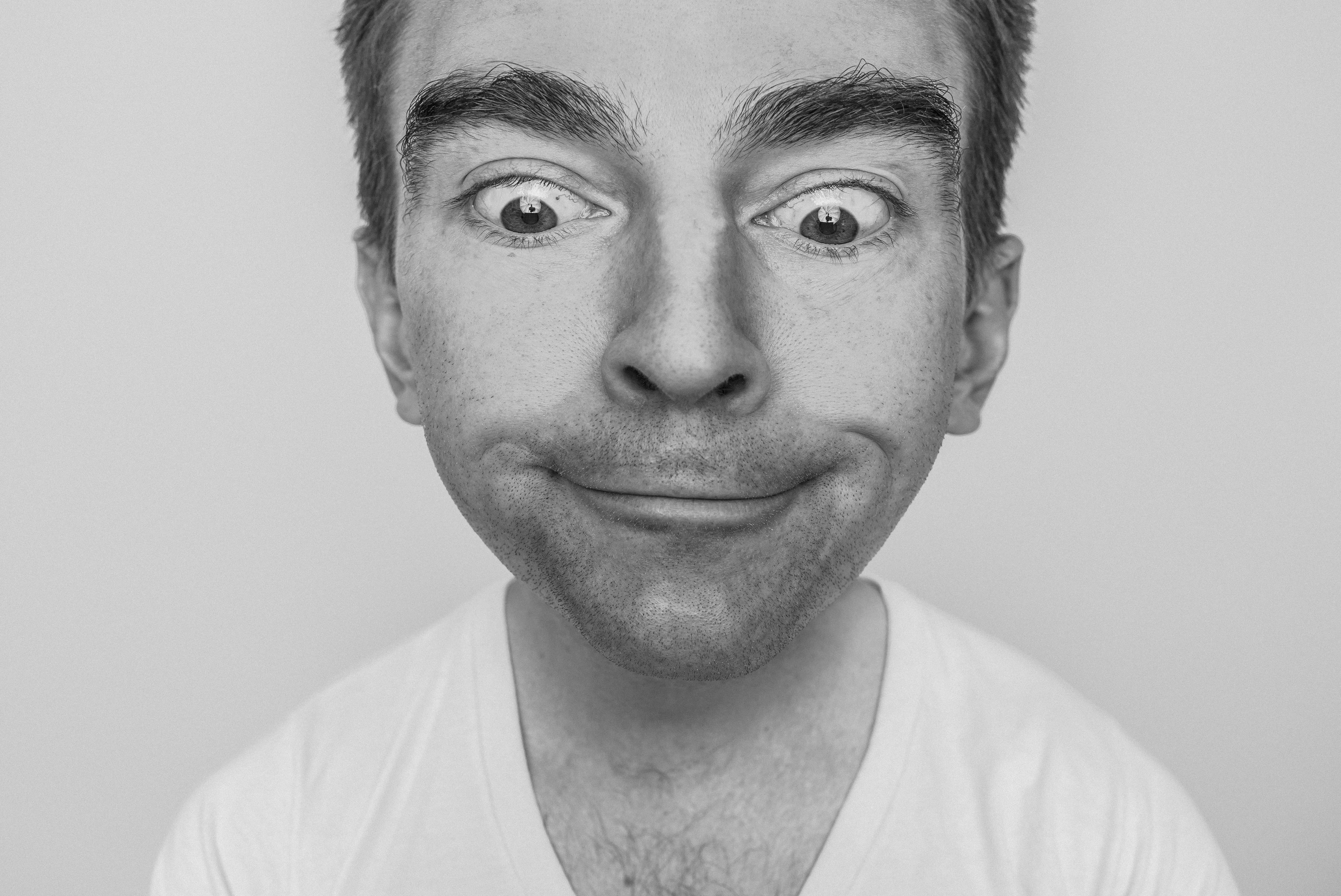 Ein Schwarz-Weiß-Porträt eines Mannes mit weit geöffneten Augen und einem schiefen Lächeln.