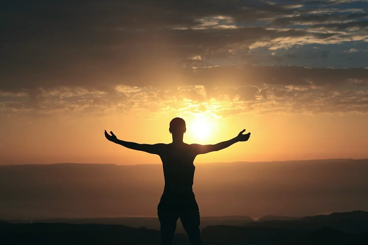 Die Silhouette eines Menschen mit ausgebreiteten Armen vor der Sonne.