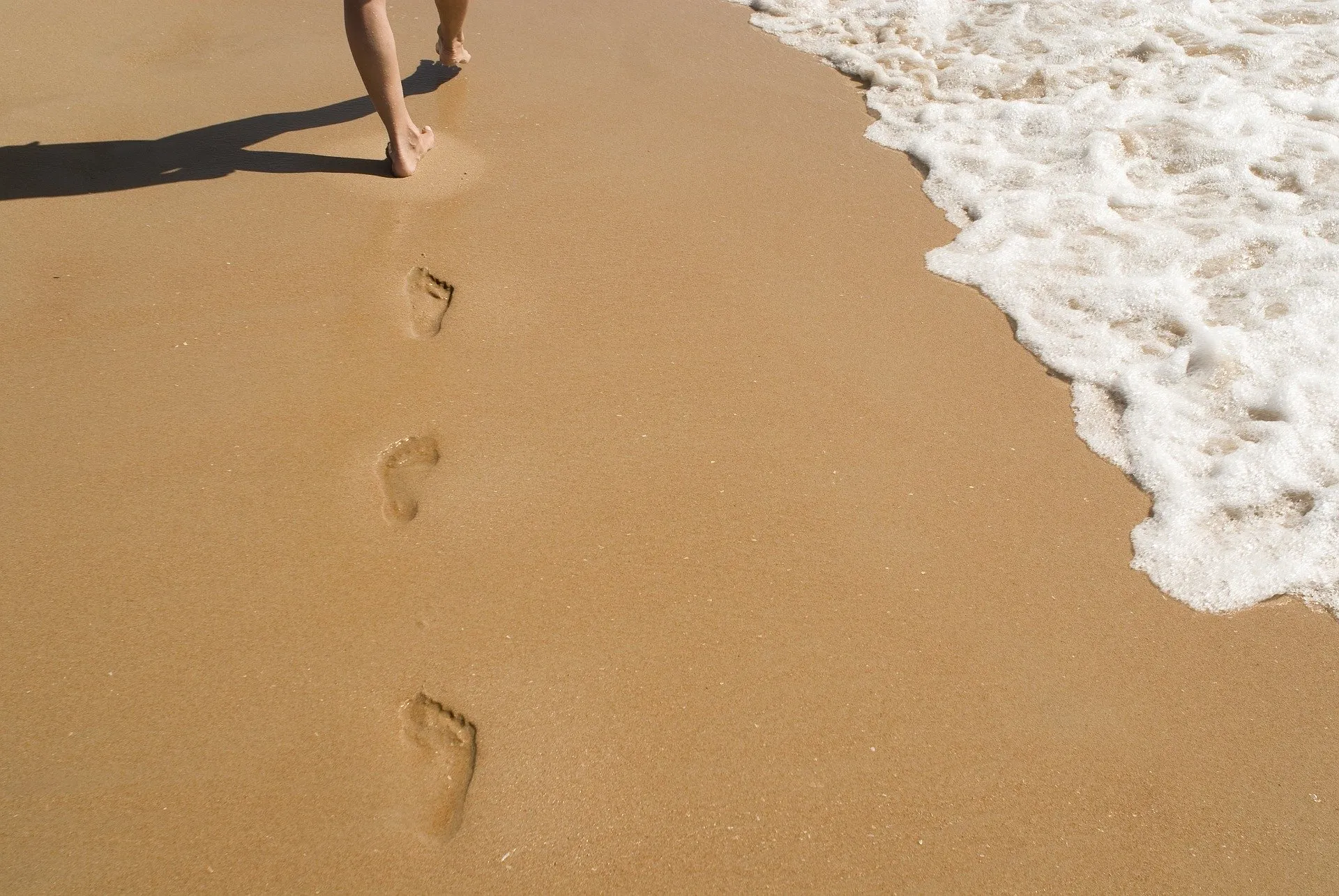 A person leaves footprints in the sand while walking beside the waves.