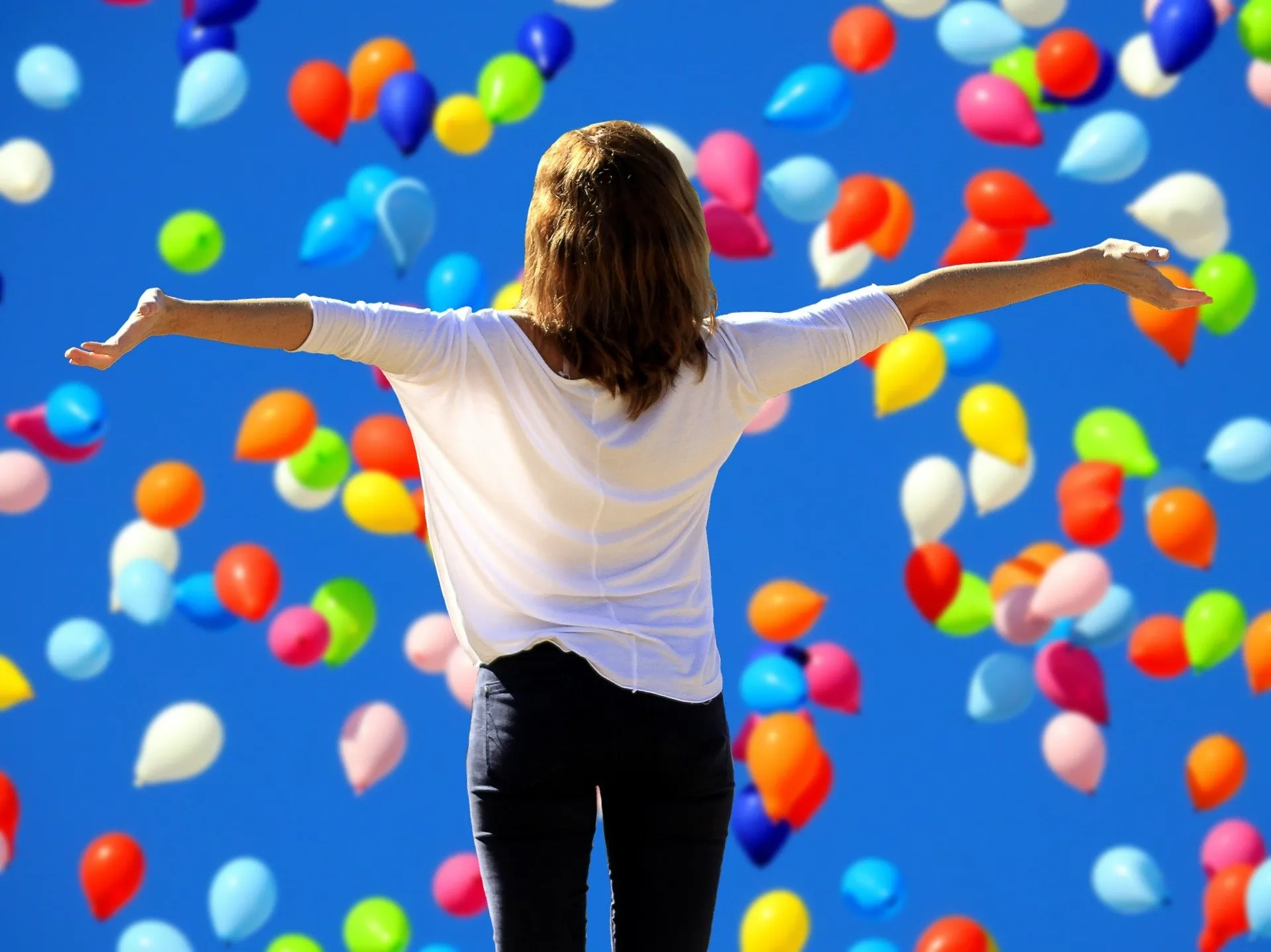 Una persona con los brazos abiertos bajo numerosos globos de colores.