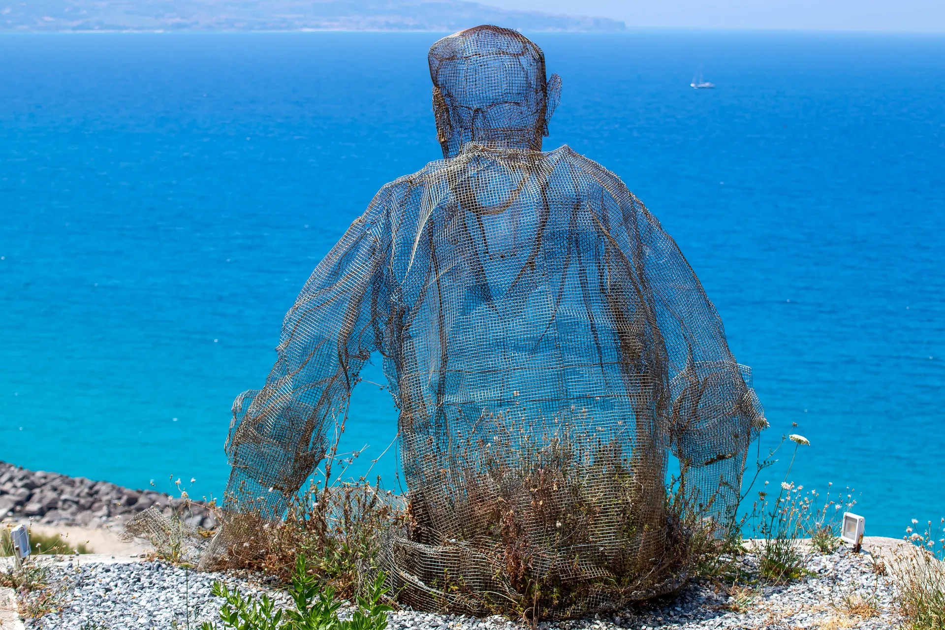 Una escultura de alambre de una persona sentada frente al mar azul.